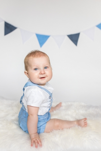 Child sitting side on in blue dungarees - smiling to camera - milestone sitter session - debbie dee photography