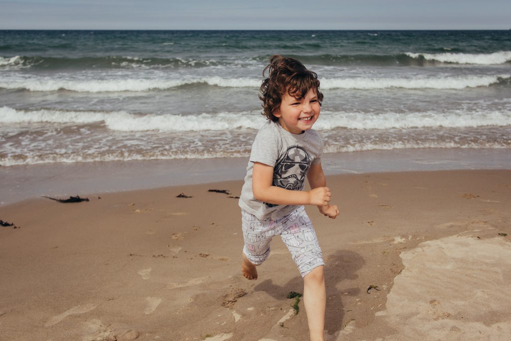 Boy running and smiling at Sandend Beach - Debbie Dee Photography - Aberdeenshire family photography